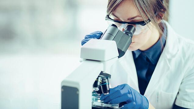Eine Wissenschaftlerin schaut in ein Mikroskop.