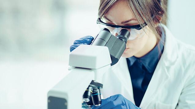 Eine Wissenschaftlerin schaut in ein Mikroskop.