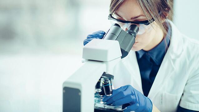 Eine Wissenschaftlerin schaut in ein Mikroskop.