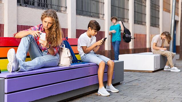 Jugendliche auf einer Bank an einem Handy