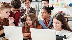 Jugendliche und eine Lehrerin arbeiten an zwei Laptops.