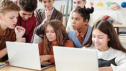 Jugendliche und eine Lehrerin arbeiten an zwei Laptops.