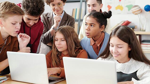 Jugendliche und eine Lehrerin arbeiten an zwei Laptops.