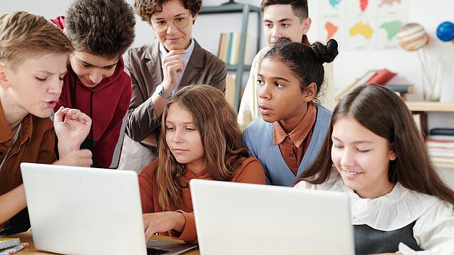 Jugendliche und eine Lehrerin arbeiten an zwei Laptops.