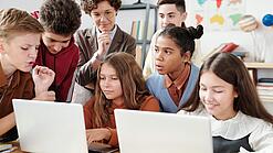 Jugendliche und eine Lehrerin arbeiten an zwei Laptops.