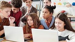 Jugendliche und eine Lehrerin arbeiten an zwei Laptops.