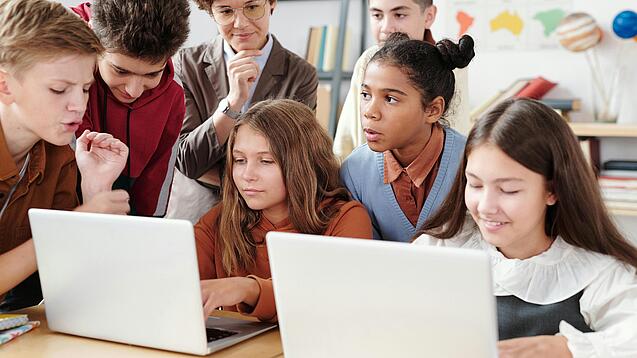 Jugendliche und eine Lehrerin arbeiten an zwei Laptops.