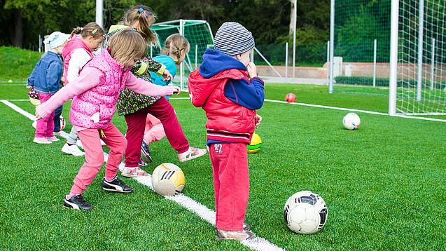 Kindergartenkinder spielen Fußball auf einem Fußballfeld.