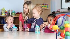 Junge Frau mit drei Kleinkindern in einer Kita.