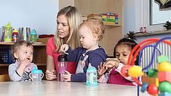 Junge Frau mit drei Kleinkindern in einer Kita.