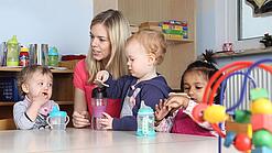 Junge Frau mit drei Kleinkindern in einer Kita.