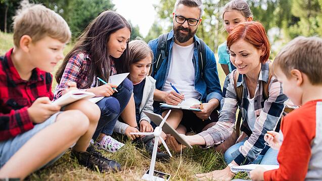 Eine Gruppe Schüler:innen sitzt mit zwei Lehrkräften um das Modell eines Windrads.