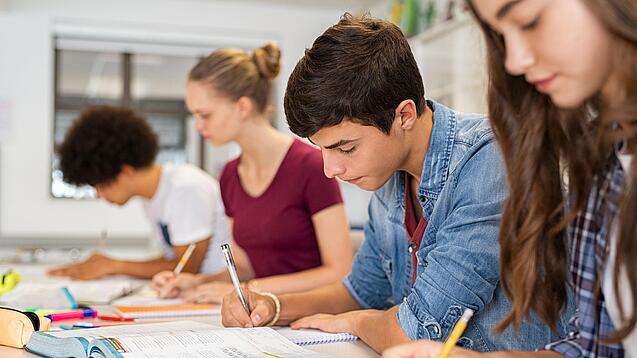 Schülerinnen und Schüler einer weiterführenden Schule sitzen im Unterricht und notieren etwas in ihren Heften.