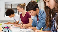 Schülerinnen und Schüler einer weiterführenden Schule sitzen im Unterricht und notieren etwas in ihren Heften.