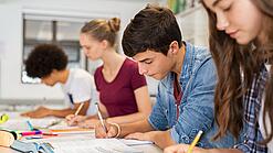Schülerinnen und Schüler einer weiterführenden Schule sitzen im Unterricht und notieren etwas in ihren Heften.