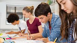Schülerinnen und Schüler einer weiterführenden Schule sitzen im Unterricht und notieren etwas in ihren Heften.