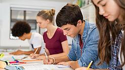 Schülerinnen und Schüler einer weiterführenden Schule sitzen im Unterricht und notieren etwas in ihren Heften.