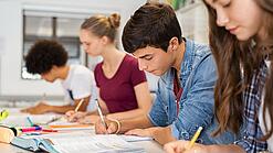 Schülerinnen und Schüler einer weiterführenden Schule sitzen im Unterricht und notieren etwas in ihren Heften.