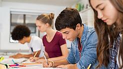 Schülerinnen und Schüler einer weiterführenden Schule sitzen im Unterricht und notieren etwas in ihren Heften.