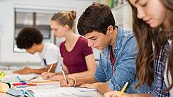 Schülerinnen und Schüler einer weiterführenden Schule sitzen im Unterricht und notieren etwas in ihren Heften.