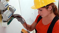 Eine Frau prüft mit einem Messgerät einen Elektroverteiler.