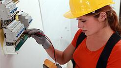 Eine Frau prüft mit einem Messgerät einen Elektroverteiler.