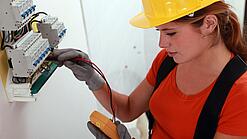 Eine Frau prüft mit einem Messgerät einen Elektroverteiler.