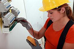 Eine Frau prüft mit einem Messgerät einen Elektroverteiler.