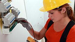 Eine Frau prüft mit einem Messgerät einen Elektroverteiler.
