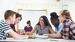 Gut gelaunte Kinder sitzen in der Schule um einen Tisch und lernen.