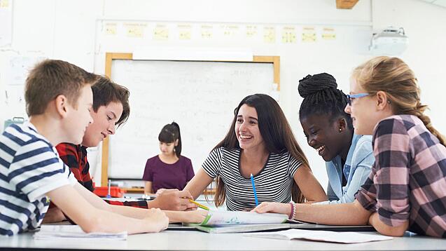 Gut gelaunte Kinder sitzen in der Schule um einen Tisch und lernen.