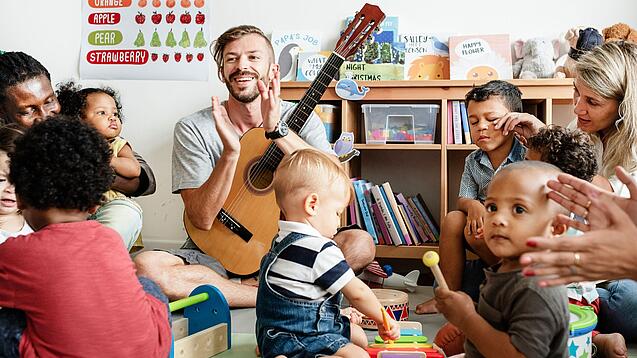 Mehrere Erwachsene und Kindergartenkinder sitzen in einem Kreis und machen gemeinsam Musik.