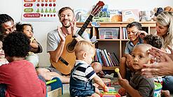 Mehrere Erwachsene und Kindergartenkinder sitzen in einem Kreis und machen gemeinsam Musik.
