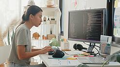 Eine junge Frau sitzt an einem großen Schreibtisch und arbeitet konzentriert an einem Computer.