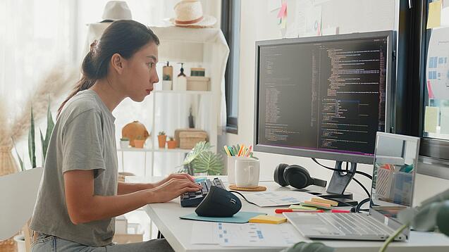 Eine junge Frau sitzt an einem großen Schreibtisch und arbeitet konzentriert an einem Computer.