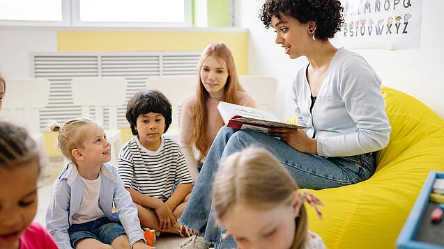 Junge Frau liest einer Gruppe Kinder etwas vor.