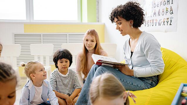 Junge Lehrerin liest einer Gruppe Schulkinder etwas vor