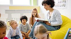 Junge Lehrerin liest einer Gruppe Schulkinder etwas vor