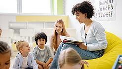 Junge Lehrerin liest einer Gruppe Schulkinder etwas vor
