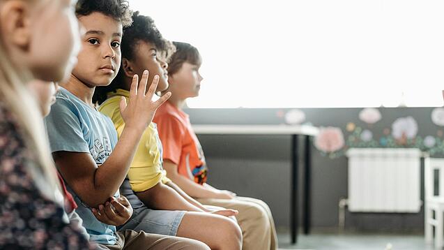 Grundschulkinder sitzen in einer Reihe in einem Klassenraum.