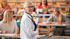 Eine Professorin steht in einem Hörsaal vor einigen Studierenden.