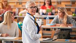 Eine Professorin steht in einem Hörsaal vor einigen Studierenden.