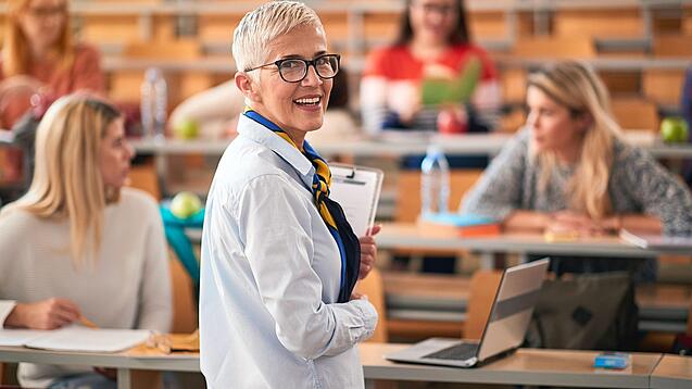 Eine Professorin steht in einem Hörsaal vor einigen Studierenden.