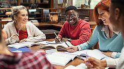 Mehrere Studierende sitzen an einem Tisch und arbeiten gut gelaunt in ihren Unterlagen.