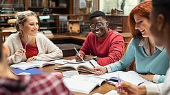 Mehrere Studierende sitzen an einem Tisch und arbeiten gut gelaunt in ihren Unterlagen.