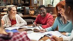 Mehrere Studierende sitzen an einem Tisch und arbeiten gut gelaunt in ihren Unterlagen.
