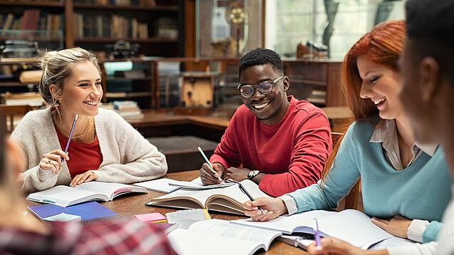 Mehrere Studierende sitzen an einem Tisch und arbeiten gut gelaunt in ihren Unterlagen.