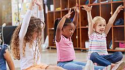 Mehrere Kita-Kinder sitzen auf dem Boden und strecken ihre Arme in die Höhe.