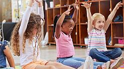 Mehrere Kita-Kinder sitzen auf dem Boden und strecken ihre Arme in die Höhe.