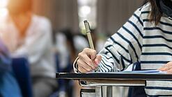 Mehrere Personen sitzen an Tischen und schreiben etwas auf.
